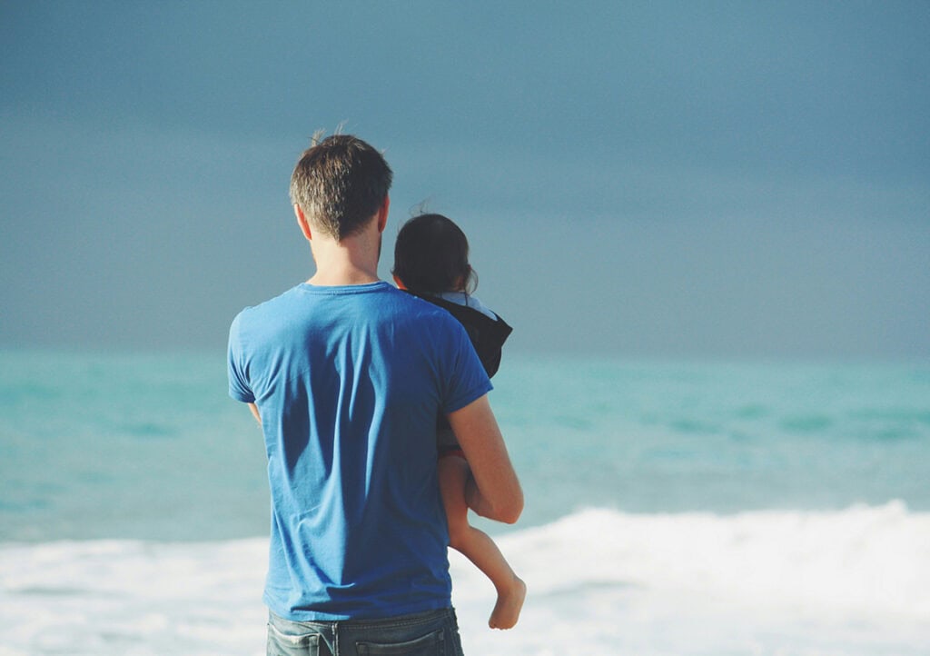 Vater mit Kind auf dem Arm schaut auf das Meer