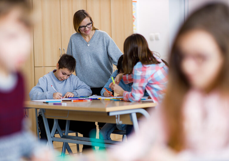 Lehrerin unterhält sich mit Schülerinnen am Tisch im Klassenraum