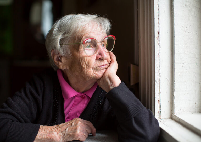 alte Frau schaut nachdenklich aus dem Fenster